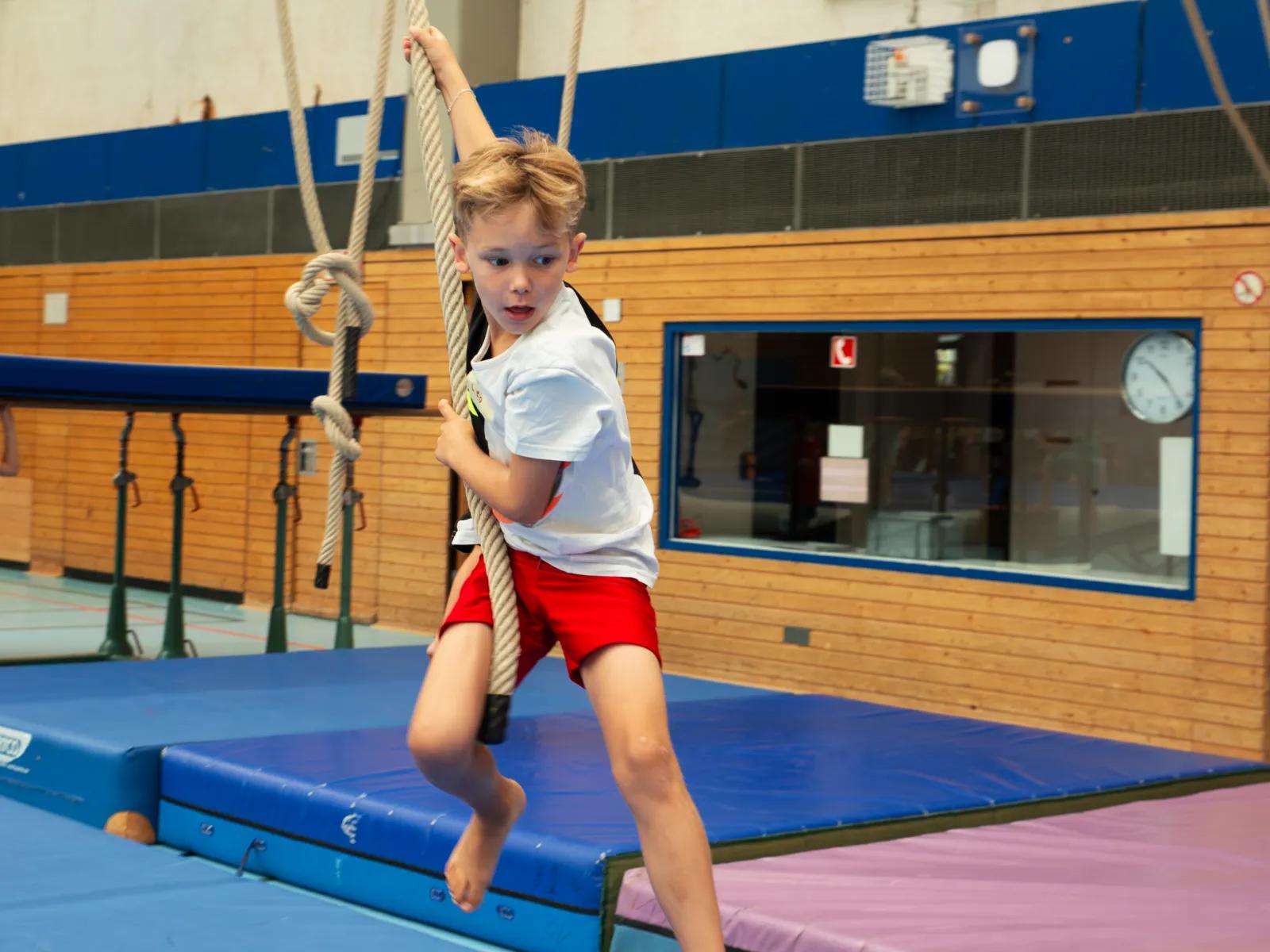 Mehrere Kinder trainieren gleichzeitig an Seilen, Kasten und Trampolin in der Halle